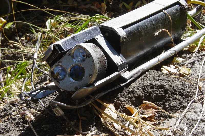 A pipe inspection camera sled with lights and lenses resting on dirt after use
