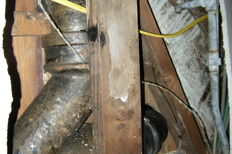 Black cast iron drain pipe with a hub joint and a wye, seen through an opening in a basement wall
