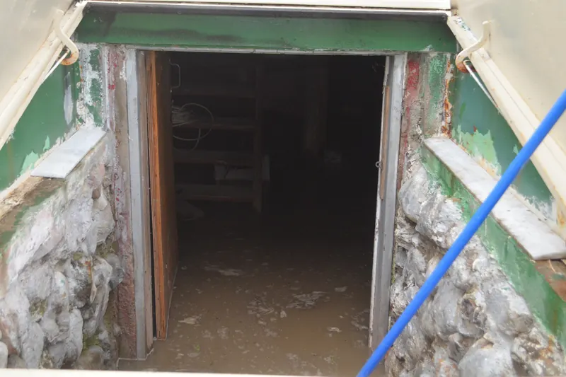 Muddy floodwater covering a basement floor, seen down a stone-walled bulkhead stairway