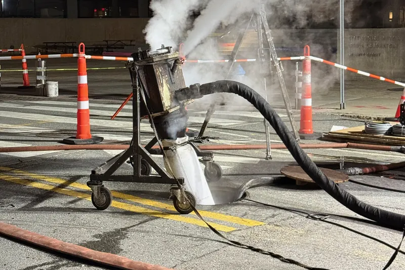 A liner inversion rig over an open manhole feeding a white liner tube into a sewer at night