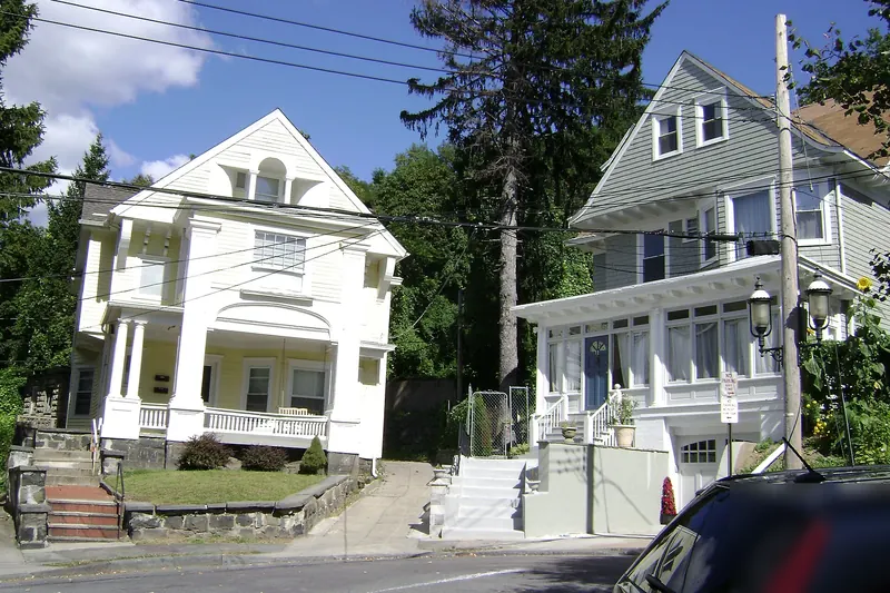 Two early-1900s frame houses with front porches on a sloping street